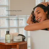 Woman in bath with Olverum bath oil and salts on table. Text: Soothes, relieves, promotes sleep.