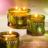 Three lit NEOM candles in green glass jars, text: "Scent to Help Uplift Mood".