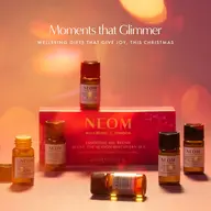 NEOM essential oil set with six small bottles on a pink surface. Text: "Moments that Glimmer".