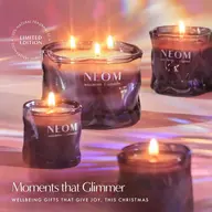 Lit NEOM candles in glass holders with text: "Moments that Glimmer".
