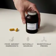 Hand holding a bottle of Wild Nutrition Daily Multi Nutrient for Teen Boys with two capsules nearby.