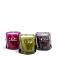 Three NEOM candles in pink, green, and purple glass jars. Text: "NEOM Wellbeing London".