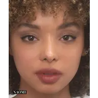 Close-up of a person with curly hair and natural makeup. Text: "NAOMI" in the corner.