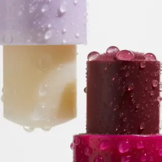 Two lipsticks with water droplets, one beige and one dark red, on a white background.