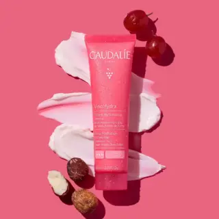Caudalie VinoHydra cream tube on pink background with grapes and shea nuts.