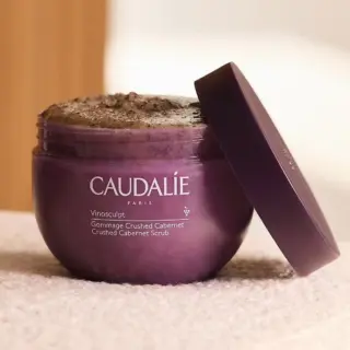 Caudalie Vinosculpt Crushed Cabernet Scrub in a purple jar with lid ajar.