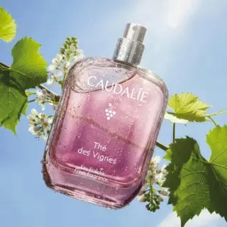 Caudalie Thé des Vignes fragrance bottle with water droplets, surrounded by green leaves and flowers.