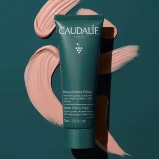 Green tube of Caudalie Instant Detox Mask on dark background with pink cream swirls.