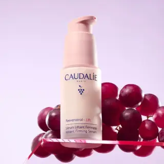 Caudalie Resveratrol Lift serum bottle with grapes on a pink background.