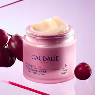 Caudalie Resveratrol Lift Firming Night Cream jar with grapes on a pink background.