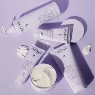 Caudalie skincare products on a purple surface, including creams and lotions.