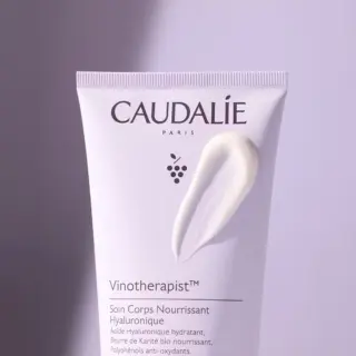 Caudalie Vinotherapist body cream tube with cream smear on a purple background.