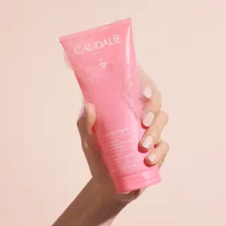 Hand holding pink Caudalie Rose de Vigne shower gel with bubbles.