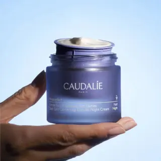 Caudalie Vinoperfect Night Cream jar held against a blue background.