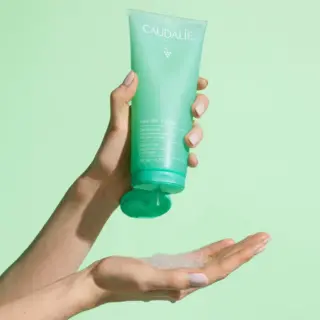 Hand holding Caudalie shower gel, dispensing onto palm against a light green background.