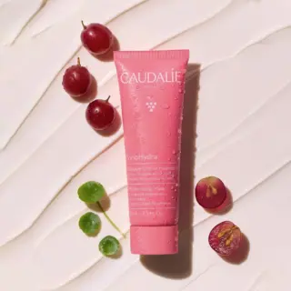 Pink Caudalie VinoHydra mask tube with grapes and leaves on a creamy background.