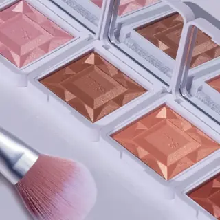 Makeup compacts with mirrors and a pink brush on a white surface.