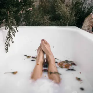 Person relaxing in an outdoor bath with milky water and scattered leaves.