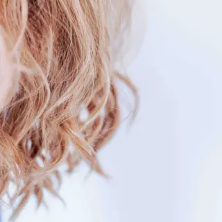 Curly blonde hair close-up against a light background.