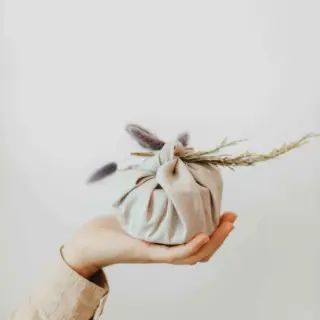 Hand holding a fabric-wrapped bundle with dried flowers on top.