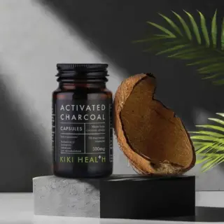 Activated charcoal capsules bottle beside a coconut shell on a grey surface.