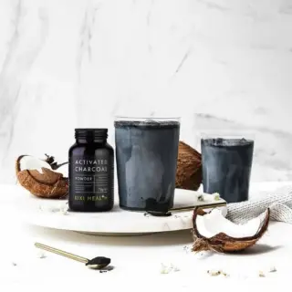 Activated charcoal powder with coconut and two charcoal drinks on a marble surface.