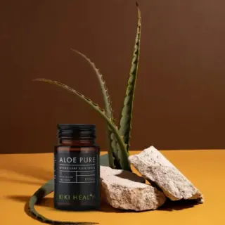 Aloe Pure capsules bottle with aloe plant and rocks on brown background.