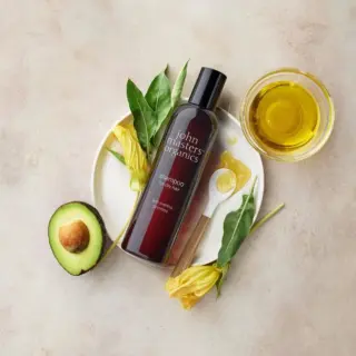 Shampoo bottle with avocado, leaves, yellow flowers, honey, and oil on a plate.