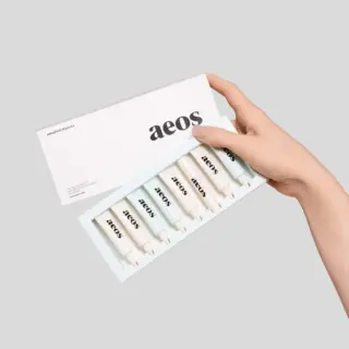Hand holding aeos skincare set with six tubes in a box.