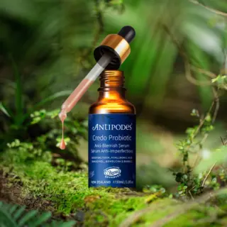 Antipodes Credo Probiotic Serum bottle with dropper in a lush green setting.