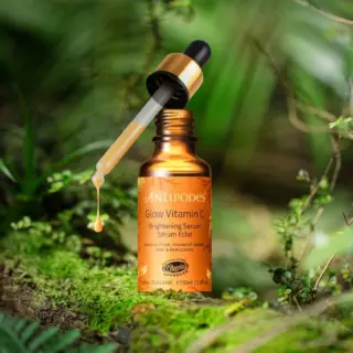 Antipodes Glow Vitamin C serum bottle with dropper in a lush green setting.