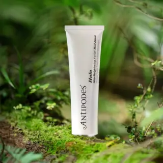Antipodes Halo Skin-Brightening Facial Mud Mask tube on a mossy forest floor.