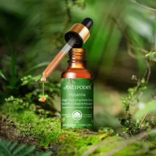 Antipodes Hosanna serum bottle with dropper, surrounded by lush green foliage.