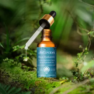 Brown bottle of Antipodes Maya Hyaluronic Serum with dropper in a lush green setting.