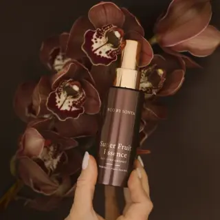 Brown bottle of Super Fruit Essence held in front of dark orchids.