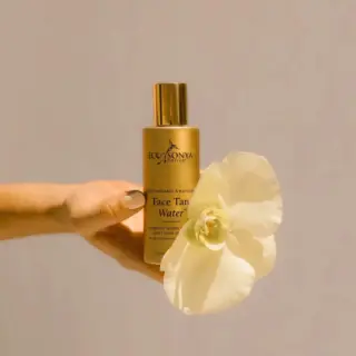 Eco by Sonya Face Tan Water bottle held with a white orchid.