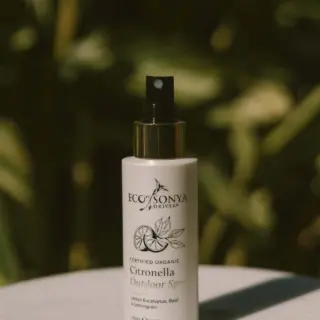 Eco Sonya Citronella Outdoor Spray bottle on a marble surface, green foliage background.