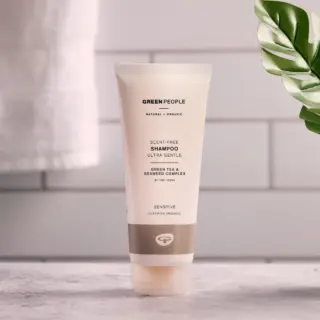 Green People scent-free shampoo tube on a bathroom counter with a plant and towel nearby.