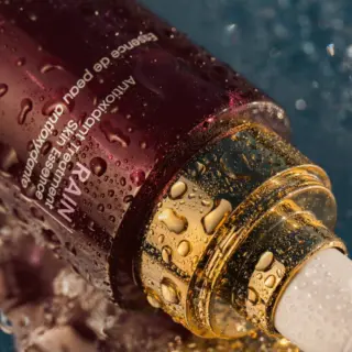 Skincare serum bottle with water droplets on a textured surface.