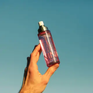 Hand holding a pink spray bottle against a clear blue sky.