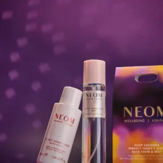 Neom Wellbeing bath foam and mist with packaging on a purple background.
