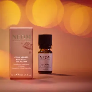 NEOM Cosy Nights Essential Oil Blend with packaging, 10ml bottle, warm bokeh background.