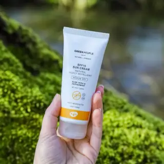 Hand holding Green People SPF15 sun cream tube outdoors.
