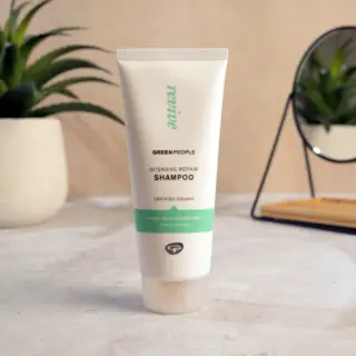 Green People Intensive Repair Shampoo tube on a bathroom counter with plants and a mirror.