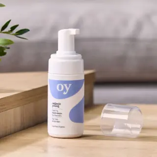 Organic Young foaming face wash on wooden surface, cap off, with plant in background.