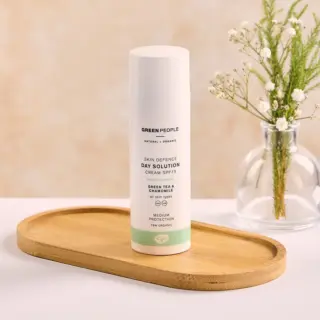 Skincare cream bottle on wooden tray, labelled "Green People Skin Defence Day Solution SPF 15".
