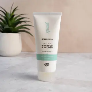 Green People Daily Aloe Shampoo & Shower tube on a marble surface, plant in background.