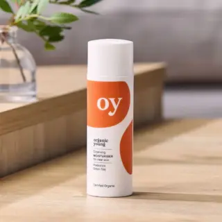 Organic Young moisturiser bottle on wooden surface, plant in background.