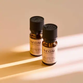 Two NEOM essential oil bottles on a beige surface with light stripes.