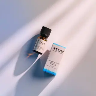 Neom essential oil bottle and box on a light surface with shadows.